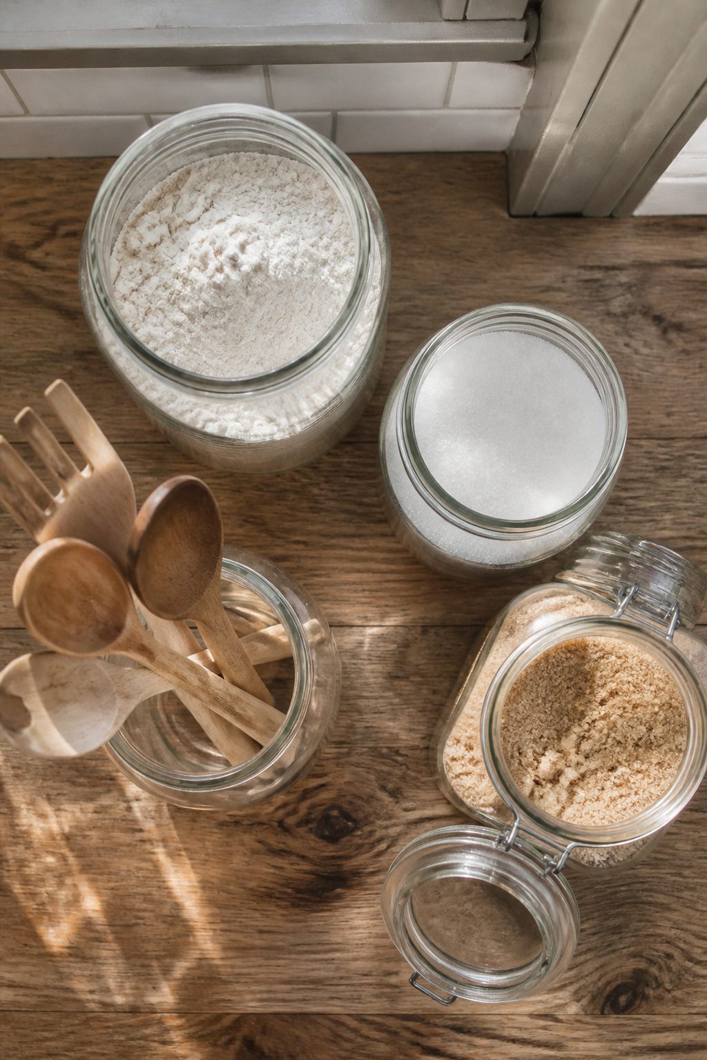 Clear mason jars filled with flour and wooden utensils on a kitchen shelf.